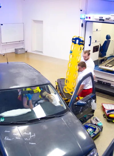 Paramedics practicing a vehicle rescue simulation with a car and ambulance in a training facility