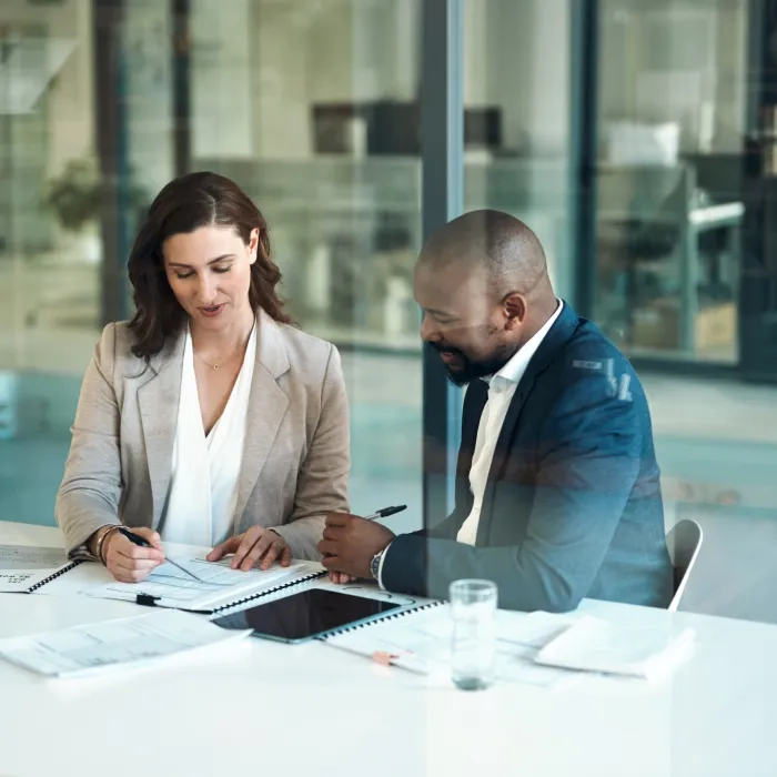 two people sitting down around a table while papers lying on the table.