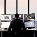 Man sitting by a desk with six monitors, monitoring the city traffic