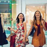 two happy women with shopping bags entering a store