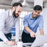 Two men smiling while pointing at a laptop