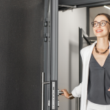 Person walking through a entrence door, wearning glasses and brown hair.