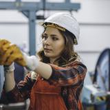 Woman, working in an industrial manufacturing, wearing a white hardhat and red pants