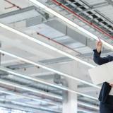 A woman and a man holding a paper and looking over a big space inside a industrial building.