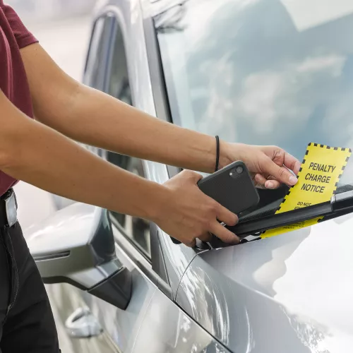 Man attaching a parking ticket onto a windshield on a car