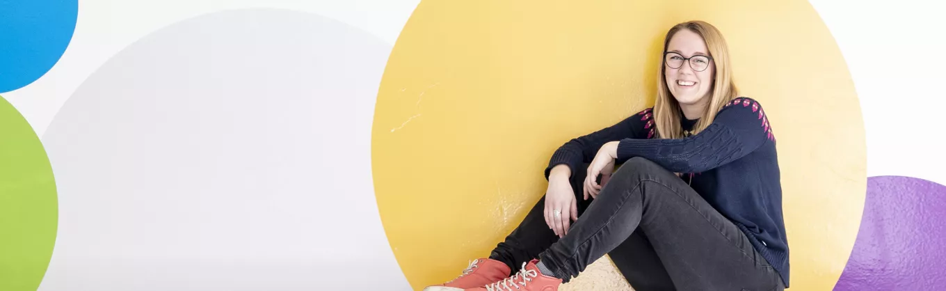 Erica Backe seated in front of a colorful, dotted wall.
