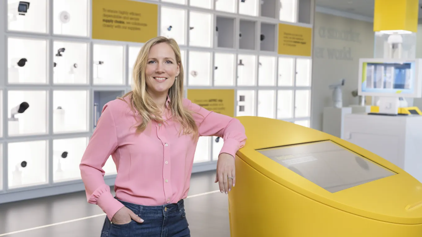 Anouska Östman is seen standing in Axis Experience Center smiling, while leaning against a yellow table.