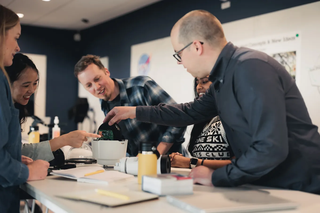 Happy Axis team members collaborating around an Axis camera placed on a table.