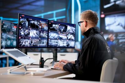 A man sitting by a desk looking at screens with surveillance footage.
