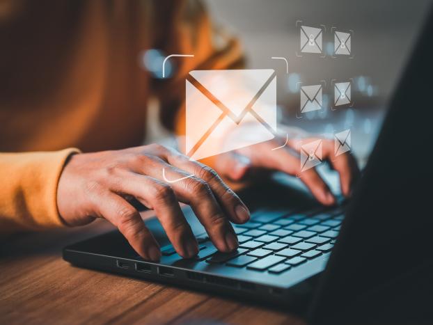 A person typing on a laptop. Visual e-mail symbols are floating above the hands.