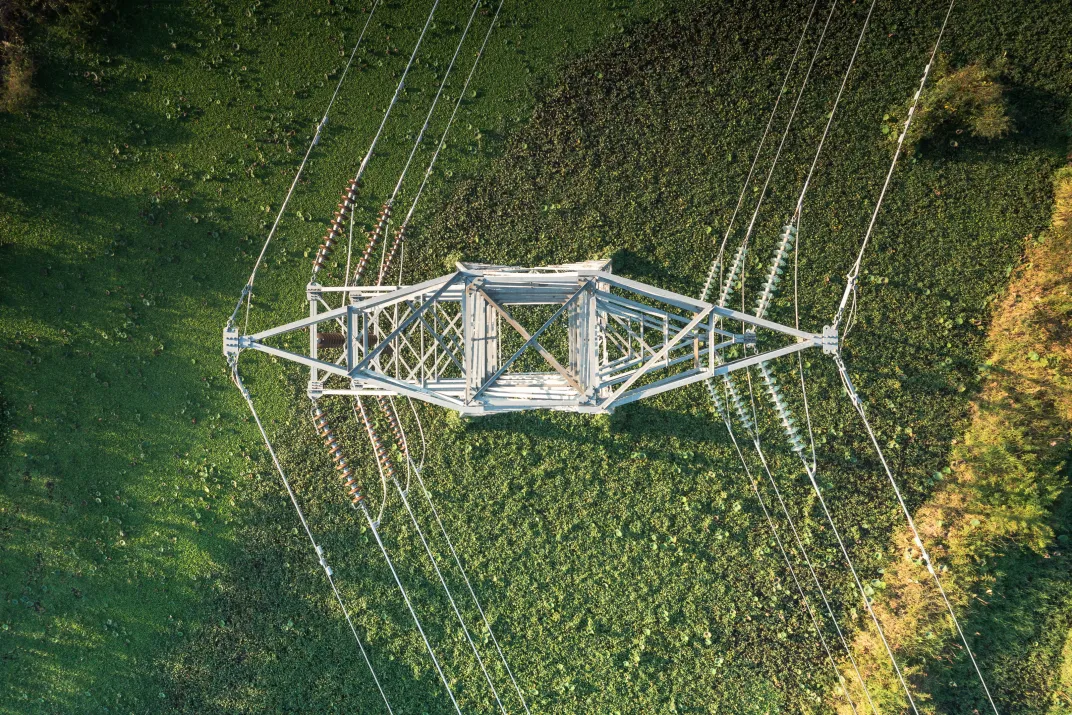 Electrical pylon transmission tower on a grass field from an aerial view.